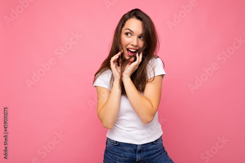 Photo portrait of young beautiful smiling hipster brunette woman in white t-shirt with mockup. Sexy carefree female person posing isolated near pink wall with empty space in studio. Positive model