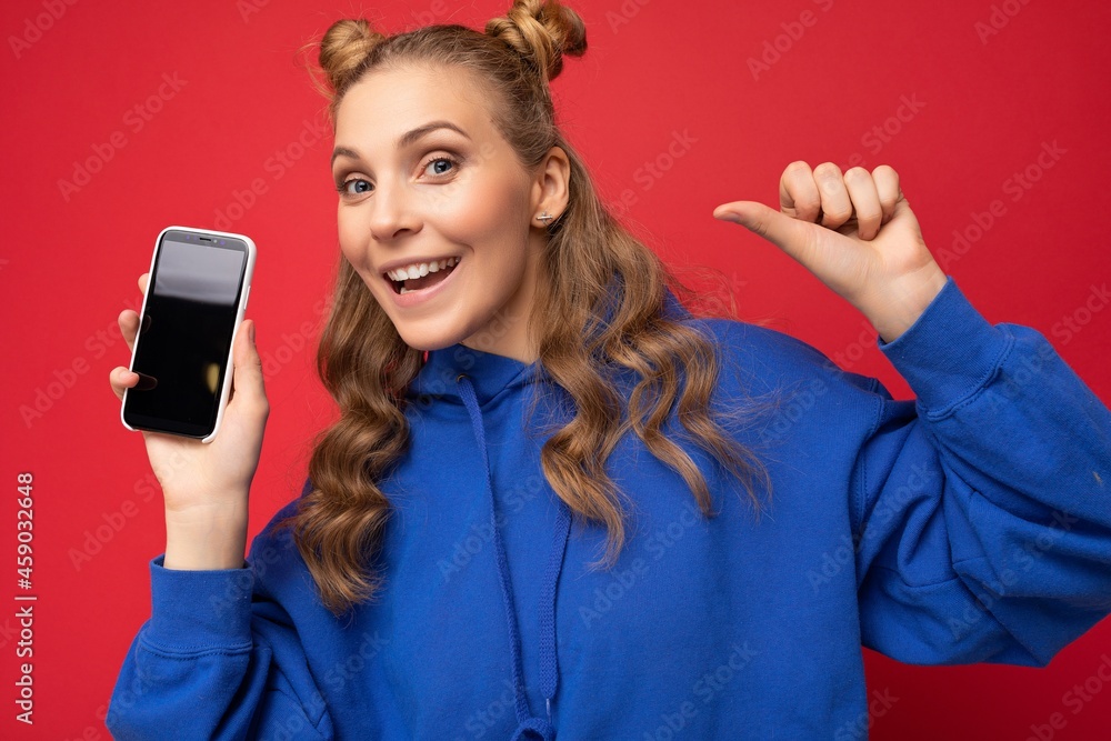 Naklejka premium Photo of beautiful smiling young woman good looking wearing casual stylish outfit standing isolated on background with copy space holding smartphone showing phone in hand with empty screen display for