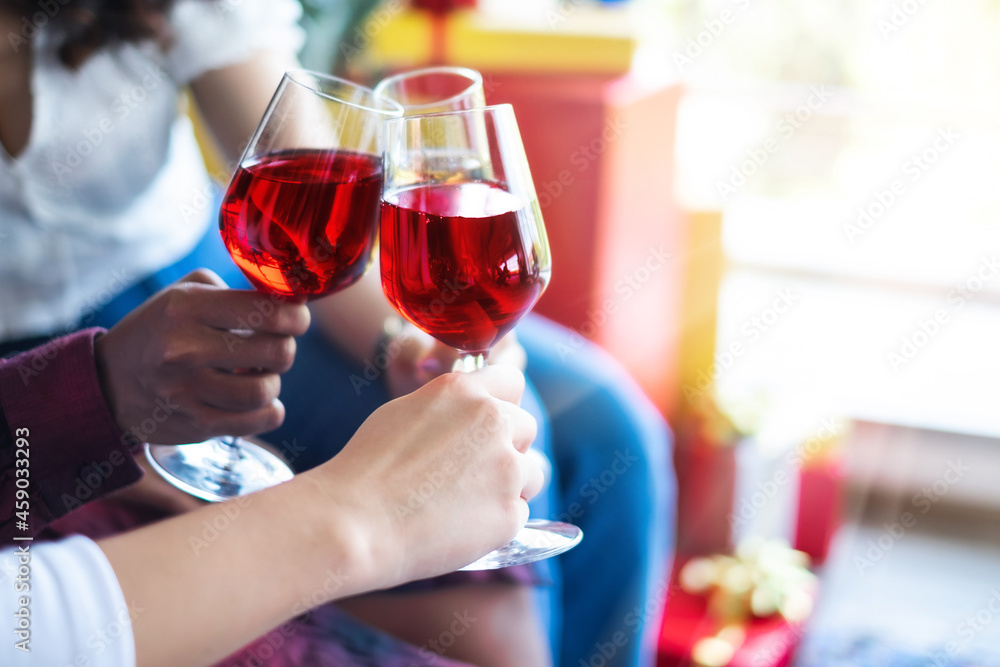 Women's hand holding glasses of red and white wine and clinking glasses in the Christmas party