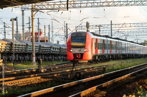 Modern russian intercity high speed passenger train on railroad at sunset, freight train on background. Commercial suburban transportation concept