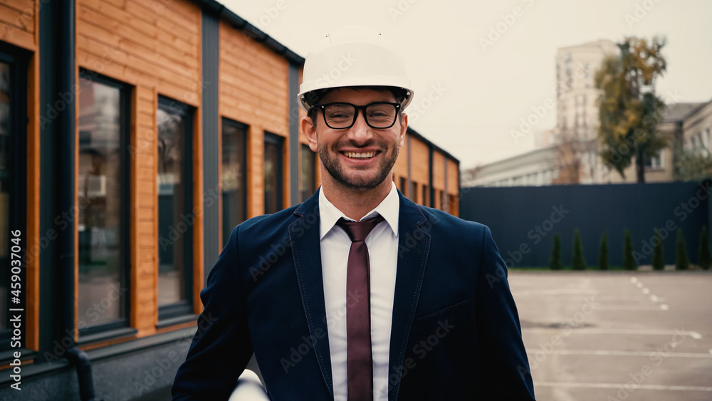 Architect in eyeglasses and helmet holding blueprint on urban street