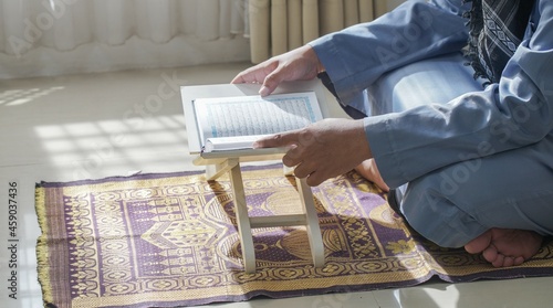 Person reading quran on stand with prayer rug. Perfect for religious, cultural, or educational content related to islam and spirituality.