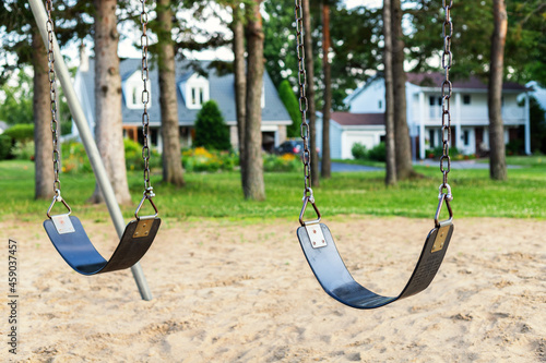 Playground with swings for children in the public park with houses in background.