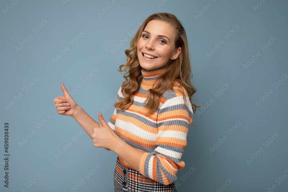Shot of young positive happy smiling blonde wavy-haired woman wearing striped pullover isolated on blue background with copy space and showing thumbs up gesture Shot of young positive happy smiling blonde wavy-haired woman wearing striped pullover isolated on blue background with copy space and showing thumbs up gesture