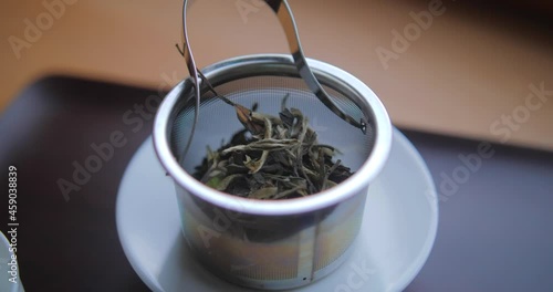 Dried Bai Mudan Tea Leaves In A Metal Teapot Filter Place On White Saucer. - close up photo