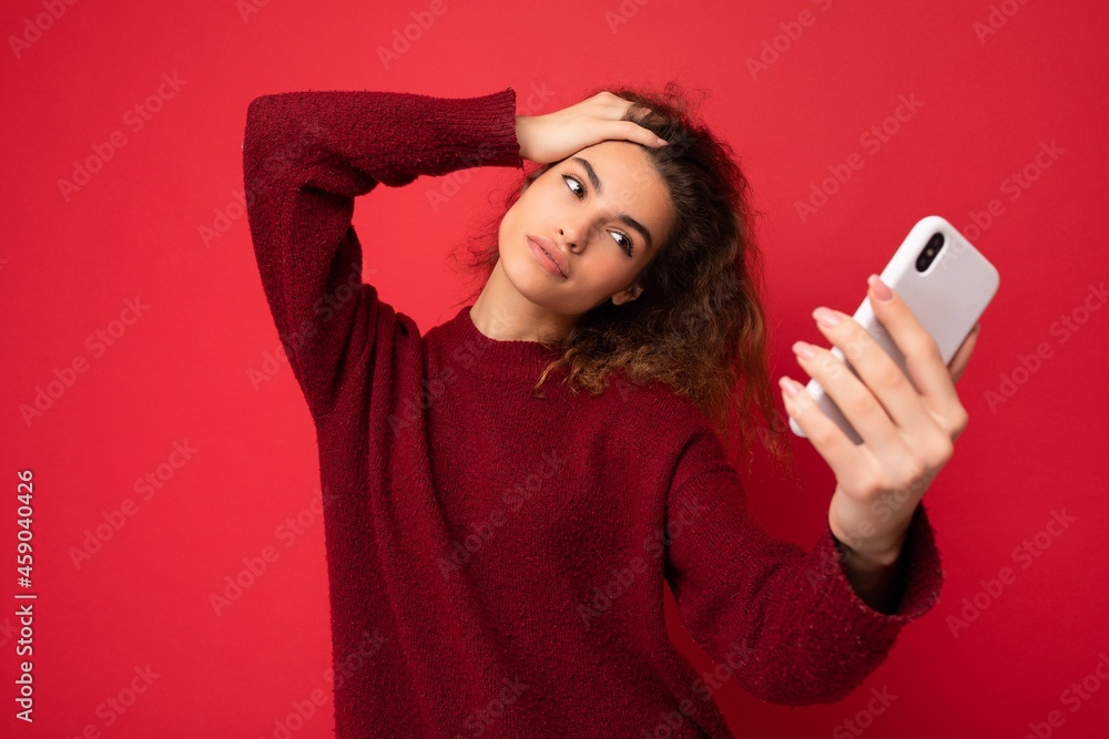 Attractive charming young smiling happy woman holding and using mobile phone taking selfie wearing stylish clothes isolated over wall background Attractive charming young smiling happy woman holding and using mobile phone taking selfie wearing stylish clothes isolated over wall background