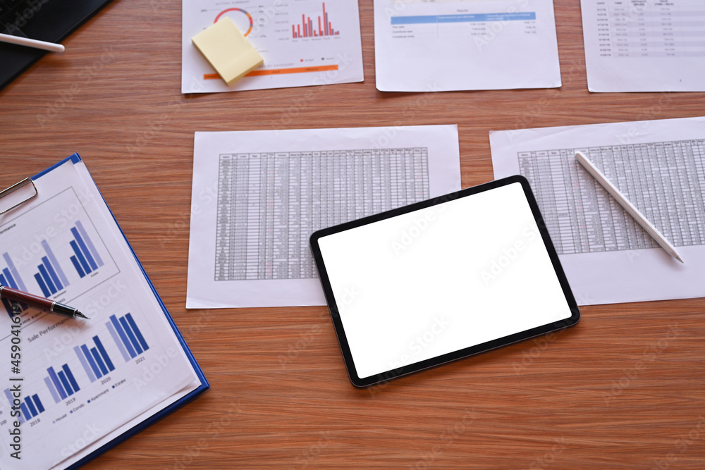 Digital tablet with white screen and financial documents on wooden office desk. Digital tablet with white screen and financial documents on wooden office desk.