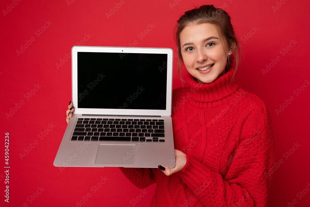 Photo of beautiful young woman holding computer laptop looking at camera isolated over colourful background Photo of beautiful young woman holding computer laptop looking at camera isolated over colourful background