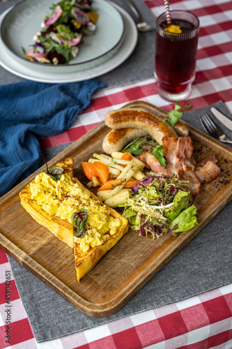 Delicious brunch platter with scramble egg toasts, grilled vegetables, salad, bacon and sausages