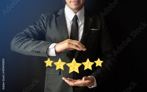 A smart bussinessman in suit is holding  a screen five gold stars (5) rating, Customer service experience and business satisfaction survey,  Feedback, review and rating concepts.tif