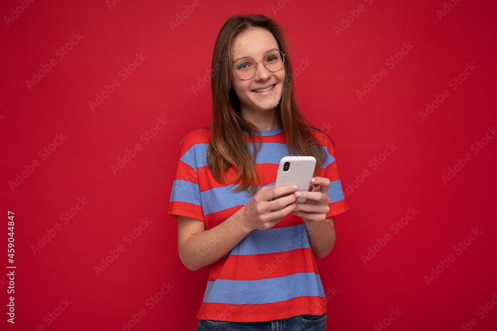 Photo shot of attractive positive good looking young woman wearing casual stylish outfit poising isolated on background with empty space holding in hand and using mobile phone messaging sms looking at Photo shot of attractive positive good looking young woman wearing casual stylish outfit poising isolated on background with empty space holding in hand and using mobile phone messaging sms looking at
