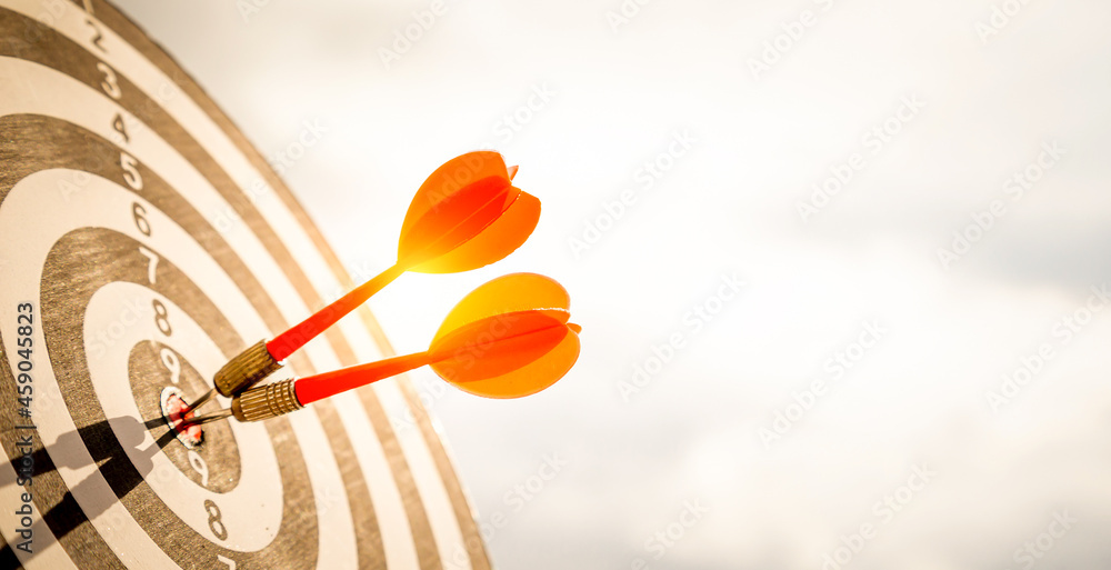 Close up shot red darts arrows in the target of dartboard center on dark blue sky background. Business target or goal success and winner concept. Close up shot red darts arrows in the target of dartboard center on dark blue sky background. Business target or goal success and winner concept.