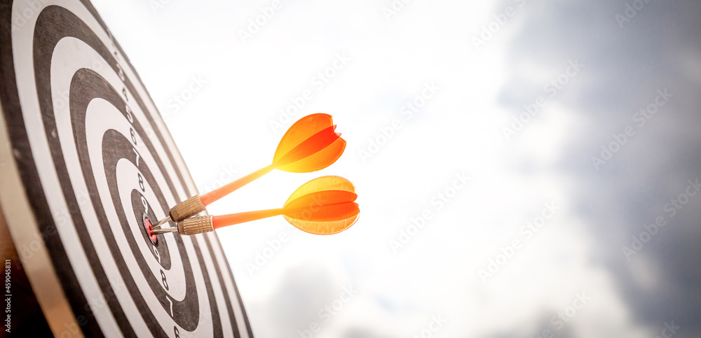 Close up shot red darts arrows in the target of dartboard center on dark blue sky background. Business target or goal success and winner concept. Close up shot red darts arrows in the target of dartboard center on dark blue sky background. Business target or goal success and winner concept.
