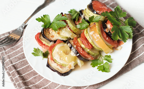 baked vegetables with cheese and parsley on a white plate, home dinner idea. vegetarian menu. sliced and roasted eggplants, tomatoes and zucchini.