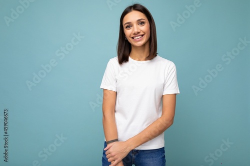 Portrait of positive cheerful fashionable smiling young brunette woman in casual white t-shirt for mockup isolated on blue background with copy space