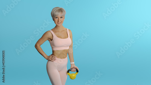 Beautiful athletic woman holding yellow kettlebell COPY SPACE BLUE BG photo