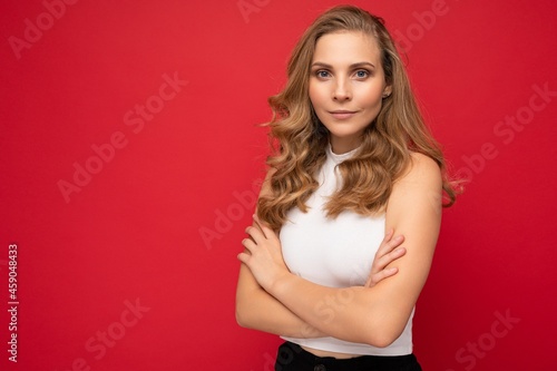 Portrait of young beautiful pretty happy confident blonde woman with sincere emotions wearing casual white top isolated over red background with empty space with arms crossed © Ivan Traimak