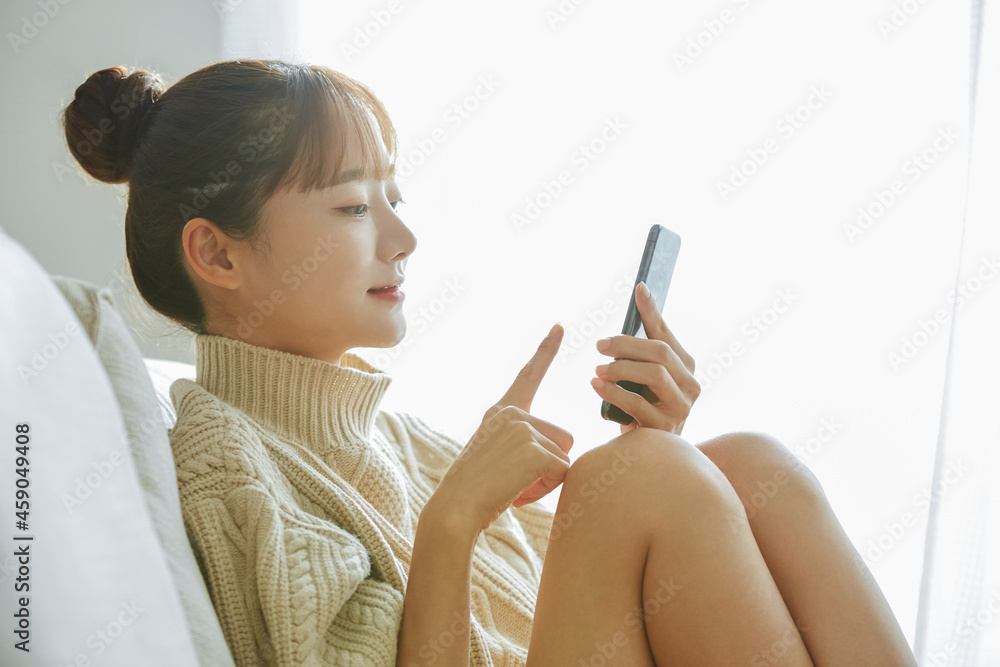 自宅でスマートフォンを操作する若い女性