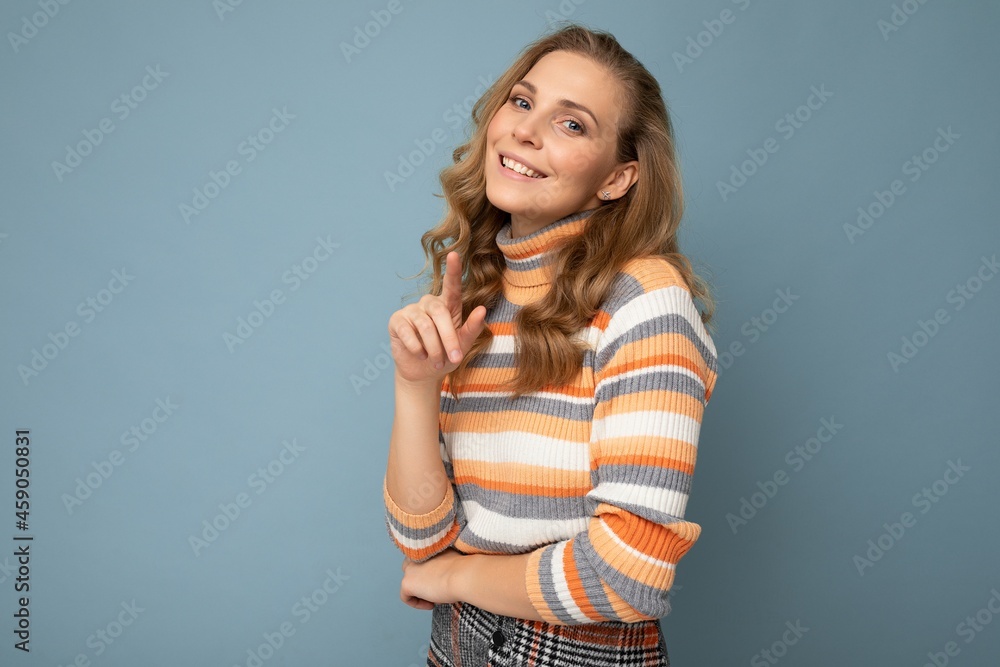 Young charming fascinating sexy positive happy smiling blonde woman wearing casual striped pullover isolated over blue background with free space and points finger at camera Young charming fascinating sexy positive happy smiling blonde woman wearing casual striped pullover isolated over blue background with free space and points finger at camera