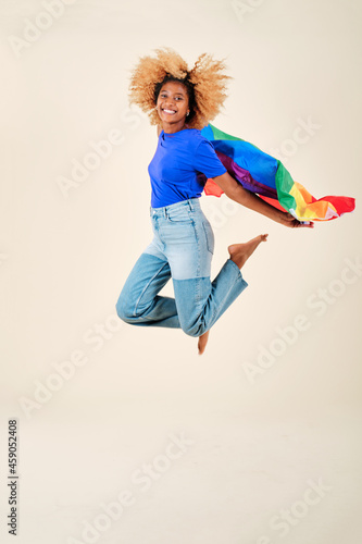 Cheerful curly hair woman jump with a gay pride flag over an isolated background.