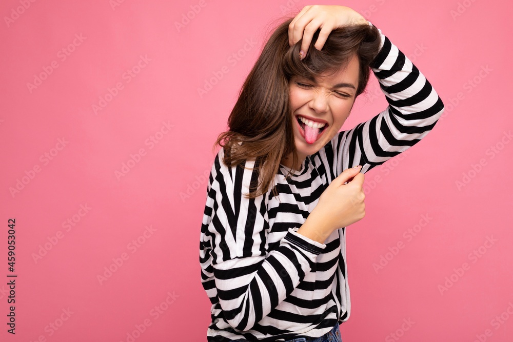Photo shot of cute attractive pretty positive happy young brunette woman wearing casual striped longsleeve isolated over colorful background with copy space and showing tongue Photo shot of cute attractive pretty positive happy young brunette woman wearing casual striped longsleeve isolated over colorful background with copy space and showing tongue