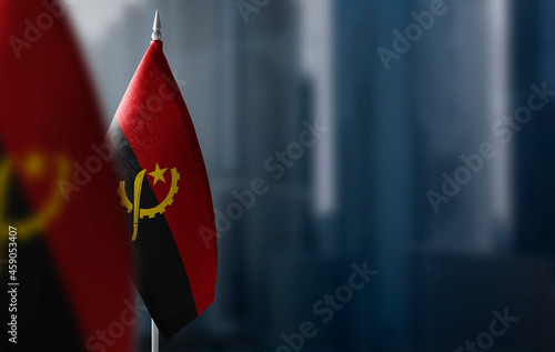 Small flags of Angola on a blurry background of the city