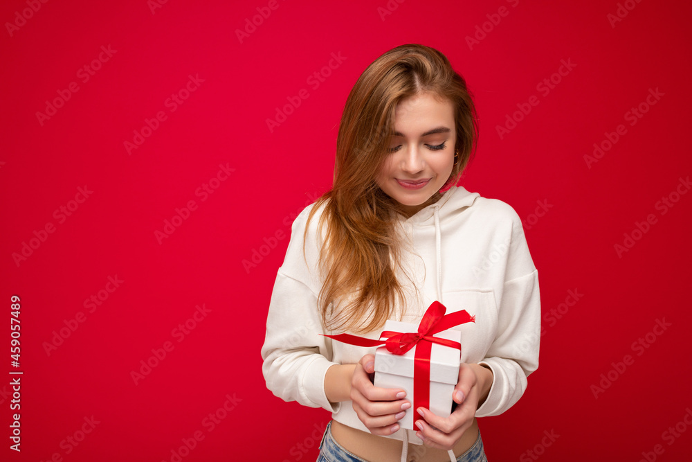 Photo shot of pretty positive surprised young dark blond woman isolated over colourful background wall wearing trendy outfit look holding gift box and looking at present box with red ribbon Photo shot of pretty positive surprised young dark blond woman isolated over colourful background wall wearing trendy outfit look holding gift box and looking at present box with red ribbon