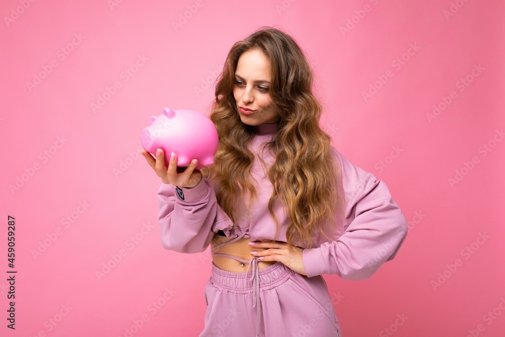 Portrait of positive doubtful thinking young beautiful attractive woman with wavy long blonde hair with sincere emotions wearing stylish pink hoodie isolated over pink background with copy space and Portrait of positive doubtful thinking young beautiful attractive woman with wavy long blonde hair with sincere emotions wearing stylish pink hoodie isolated over pink background with copy space and