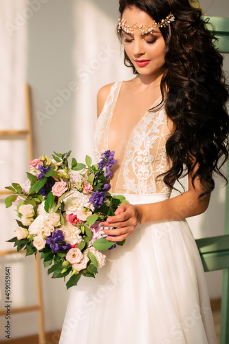 Beautiful young woman in a sexy dress Portrait of a brunette with flowers in her hands and jewelry on her head
