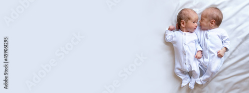 Newborn twins on the bed, in the arms of their parents, on a white background. Life style, emotions of kids. Banner