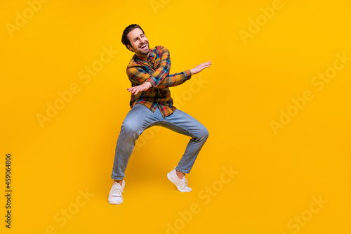 Full body photo of lovely brunet young guy dance wear shirt jeans sneakers isolated on yellow background