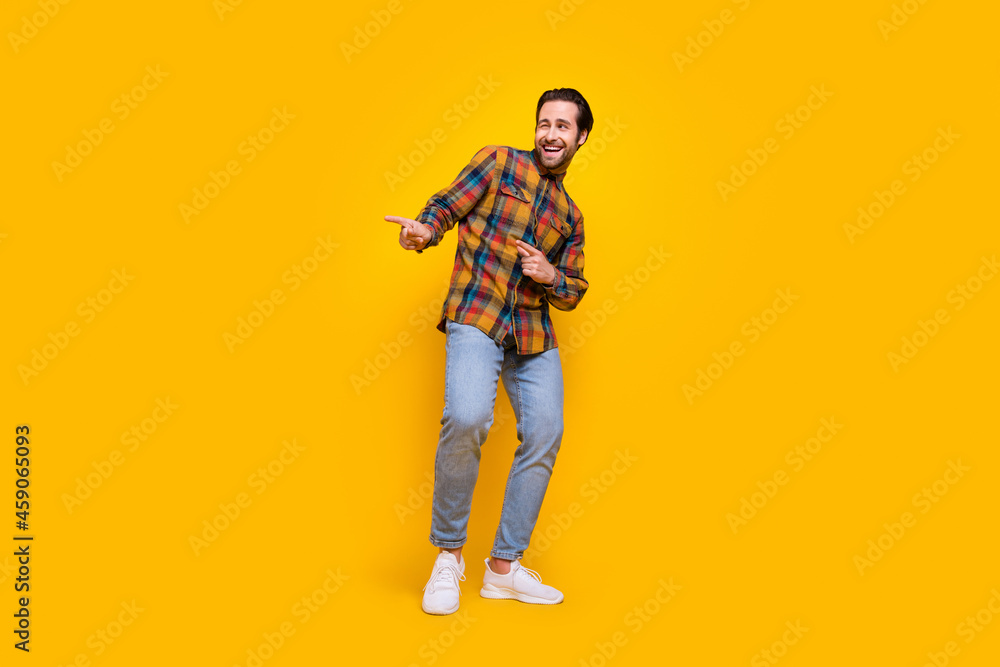 Full length photo of cool brunet young guy point empty space wear shirt jeans sneakers isolated on yellow background Full length photo of cool brunet young guy point empty space wear shirt jeans sneakers isolated on yellow background