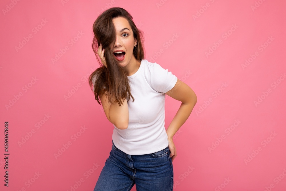 Young beautiful brunet woman. Trendy lady in casual summer white t-shirt for mock up. Positive female shows facial sincere emotions. Funny model isolated on pink background with free space Young beautiful brunet woman. Trendy lady in casual summer white t-shirt for mock up. Positive female shows facial sincere emotions. Funny model isolated on pink background with free space