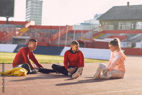 A group of young athletes is sitting on the race track and warming-up before a training at the stadium. Sport, athletics, athletes