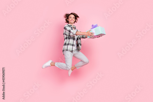 Full length photo of funky millennial brunette lady jump give present wear shirt trousers shoes isolated on pink background