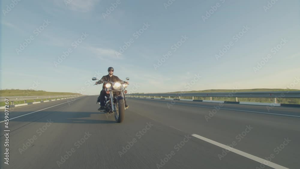 Man in helmet and sunglasses rides motorbike on road, front view. Biker on motorcycle rides highway during day in steppe background sky Man in helmet and sunglasses rides motorbike on road, front view. Biker on motorcycle rides highway during day in steppe background sky