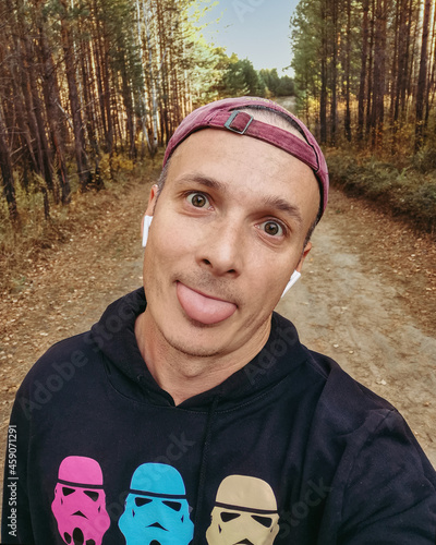 sporty man in a sweatshirt, baseball cap and headphones in the woods. Funny selfie portrait.