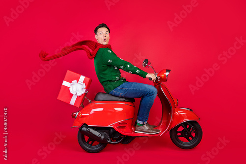 Full length body size photo man amazed crazy on bike wearing scarf delivering gift isolated vivid red color background