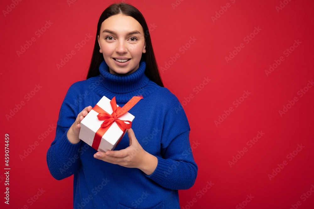 Shot of attractive positive smiling young brunette woman isolated over colourful background wall wearing everyday trendy outfit holding gift box and looking at camera Shot of attractive positive smiling young brunette woman isolated over colourful background wall wearing everyday trendy outfit holding gift box and looking at camera