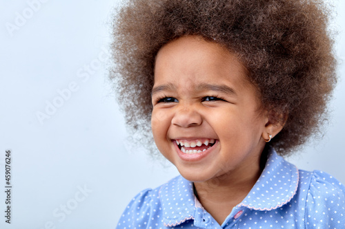 Close up portrait of little adorable African american child girl looking at side, having fun laughing isolated over white studio background. Copy space for advertisement. Human emotions, children