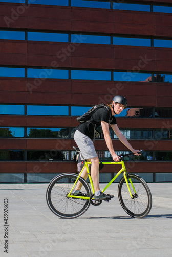 young men in a helmet on a yellow bike - Fxed gear - in the city, on the background of the building