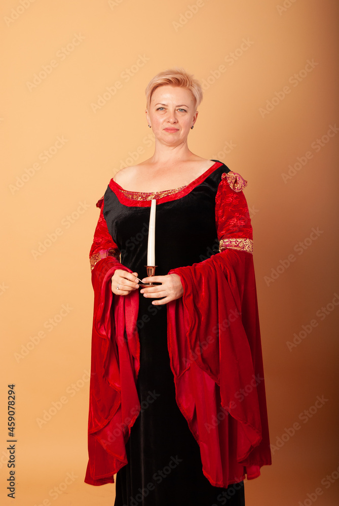 a woman in a vampire on a beige background in isolation with a glass in her hands depicts blood for Halloween