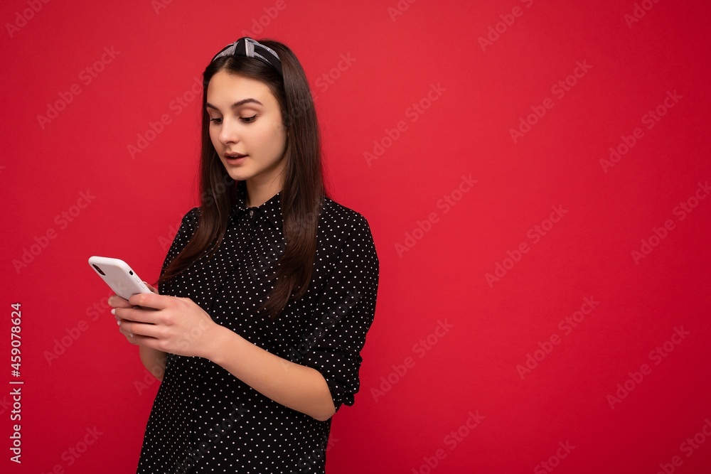 Naklejka premium Beautiful young girl wearing casual clothes standing isolated over background surfing on the internet via phone looking at mobile screen
