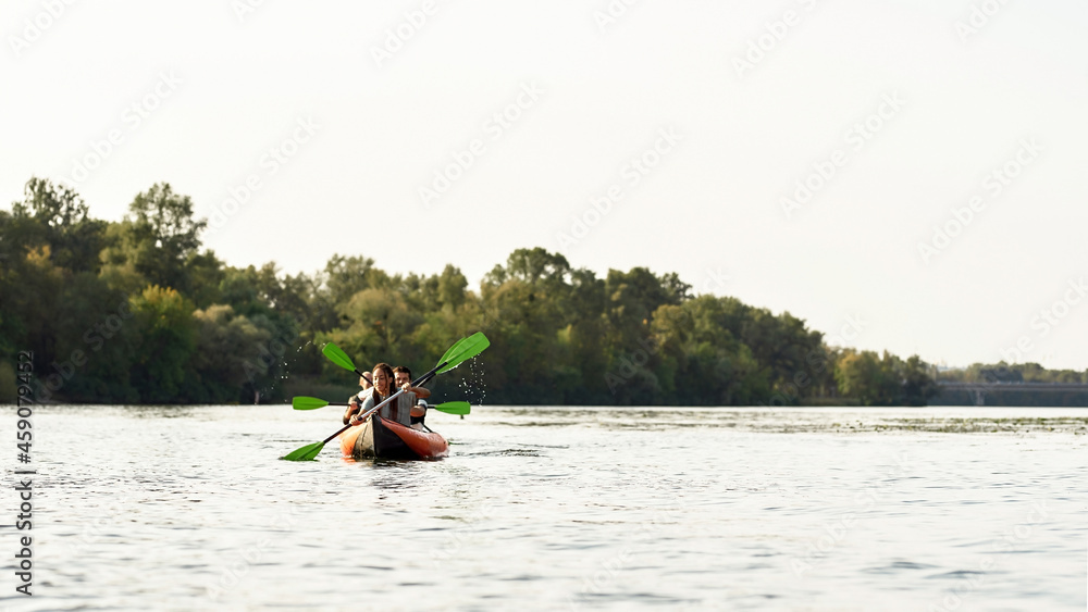 Active young people paddling together on a river surrounded by summer nature on a weekend