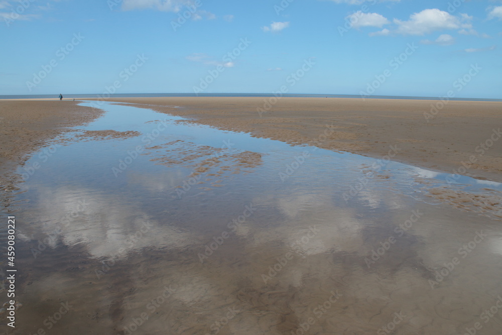 Landscape of beautiful sandy beach with no people and sands stretched to horizon with white puffy clouds reflected in the water pools in Holkham north Norfolk East Anglia uk