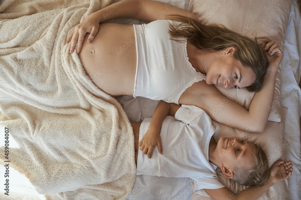 little son and his pregnant mother are lying in bed together. little son and his pregnant mother are lying in bed together.