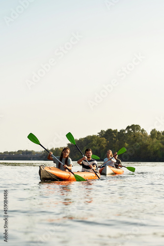 Sportive young friends paddling together on a river, spending weekend outdoors on a summer day