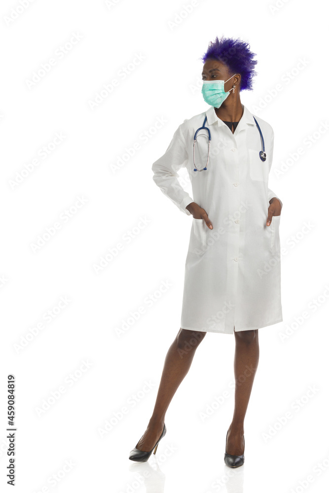 African American Female Doctor In Protective Face Mask Is Standing With Hands In Pockets And Looking Away. Full Length, Isolated. African American Female Doctor In Protective Face Mask Is Standing With Hands In Pockets And Looking Away. Full Length, Isolated.