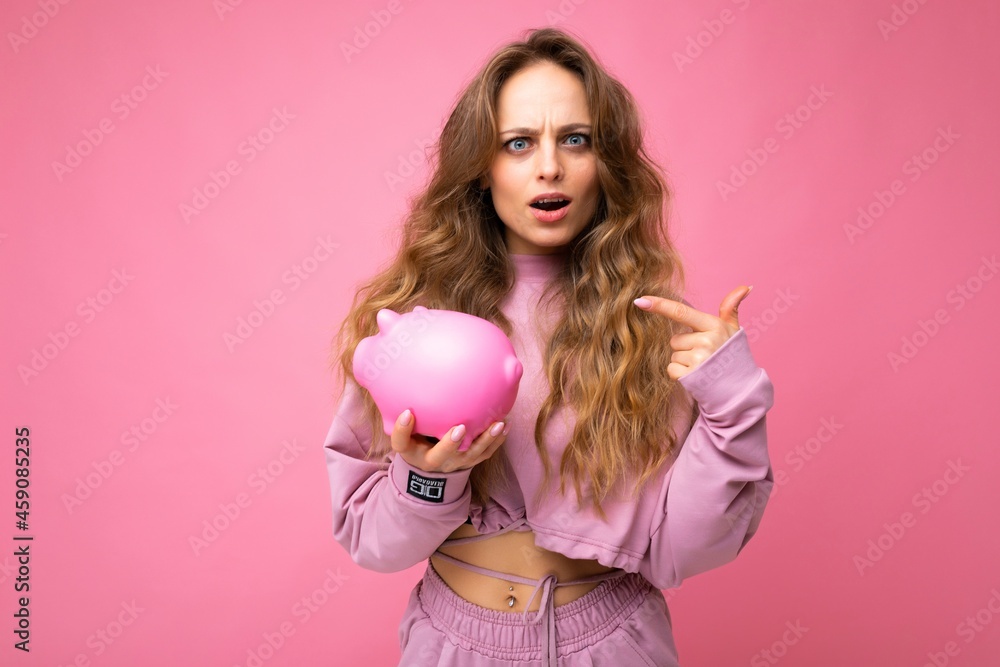 Portrait of amazes shocked surprised young charming beautiful woman with wavy long blonde hair with sincere emotions wearing stylish pink hoodie isolated over pink background with copy space, holds Portrait of amazes shocked surprised young charming beautiful woman with wavy long blonde hair with sincere emotions wearing stylish pink hoodie isolated over pink background with copy space, holds