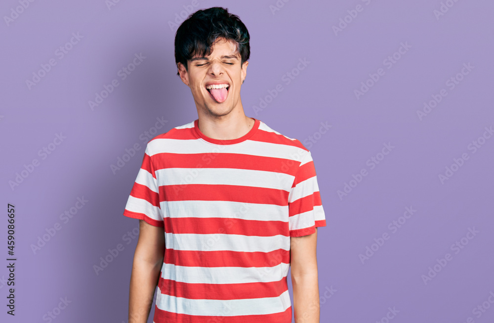 Handsome hipster young man wearing casual striped t shirt sticking tongue out happy with funny expression. emotion concept. Handsome hipster young man wearing casual striped t shirt sticking tongue out happy with funny expression. emotion concept.